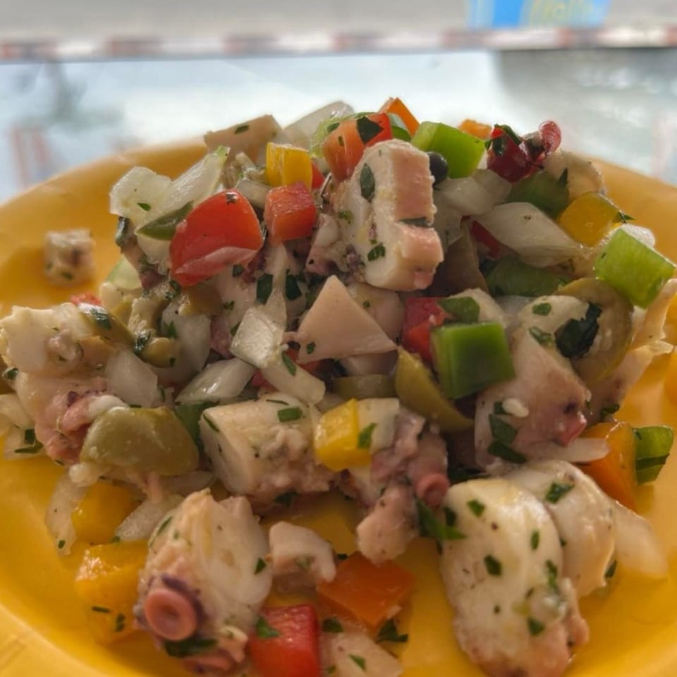 Mambo Nando's octopus salad with colorful peppers, onions, and olives on a yellow plate.
